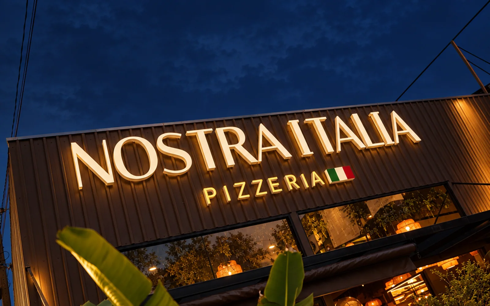 Fachada noturna da Nostra Italia Pizzeria após o rebranding
